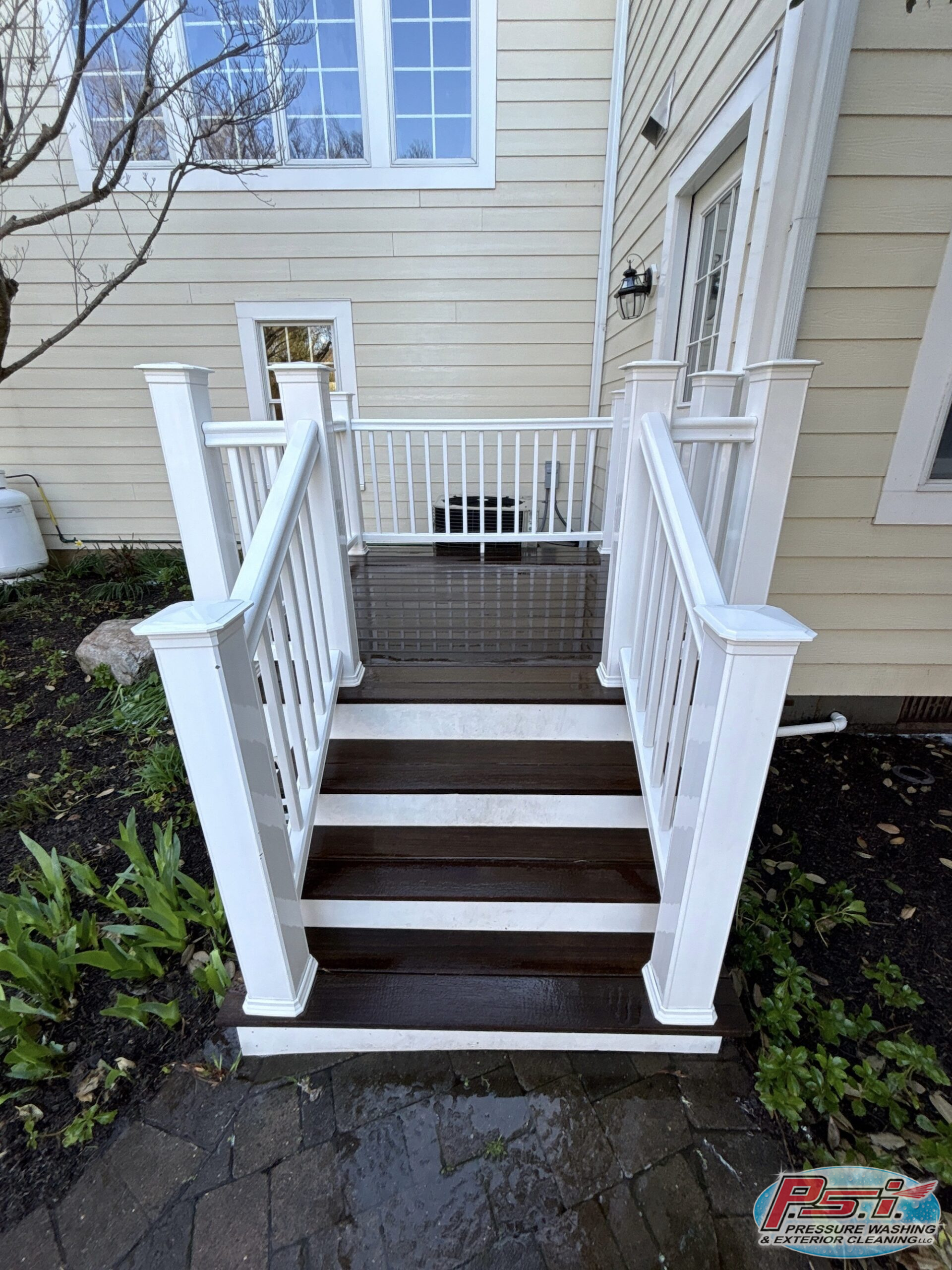 White wooden staircase with railings leads to a beige house with a glass door and lantern light.