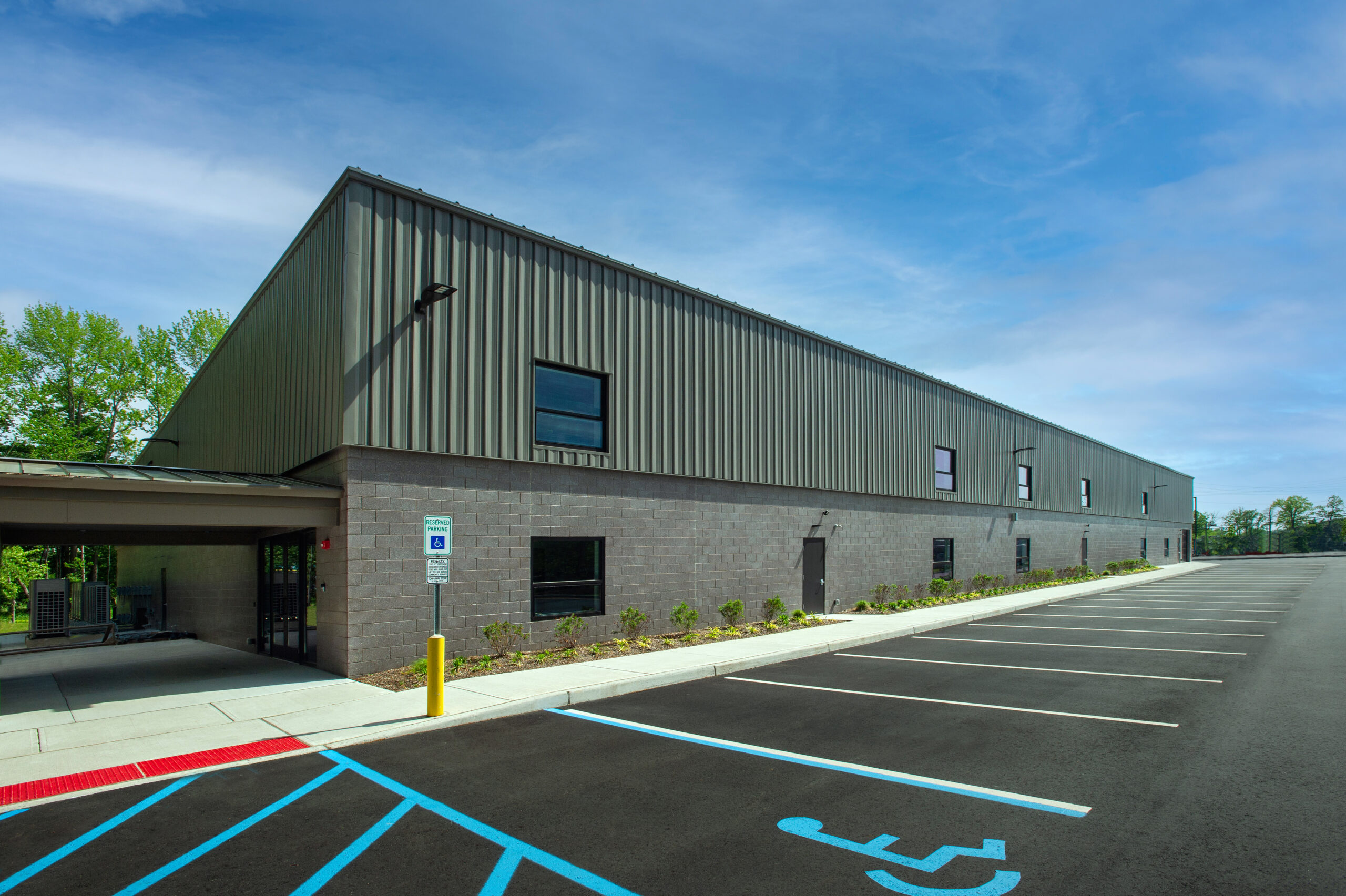 Modern warehouse-style building with metal siding under a blue sky and a row of handicap parking spaces in the foreground.