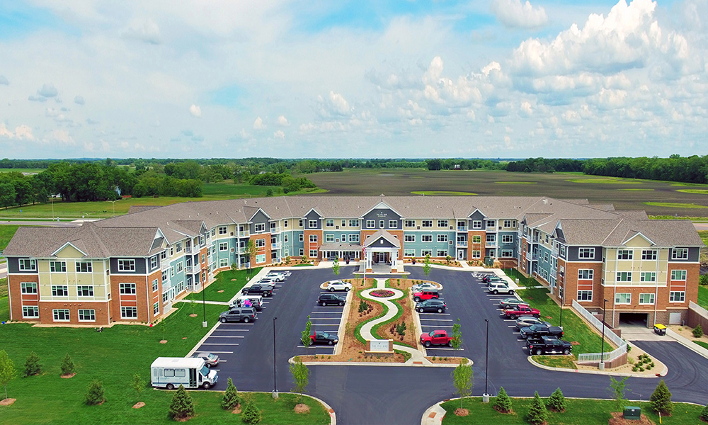 Aerial view of a U-shaped apartment complex with pastel facades, a central landscaped island, and surrounding parking lots.