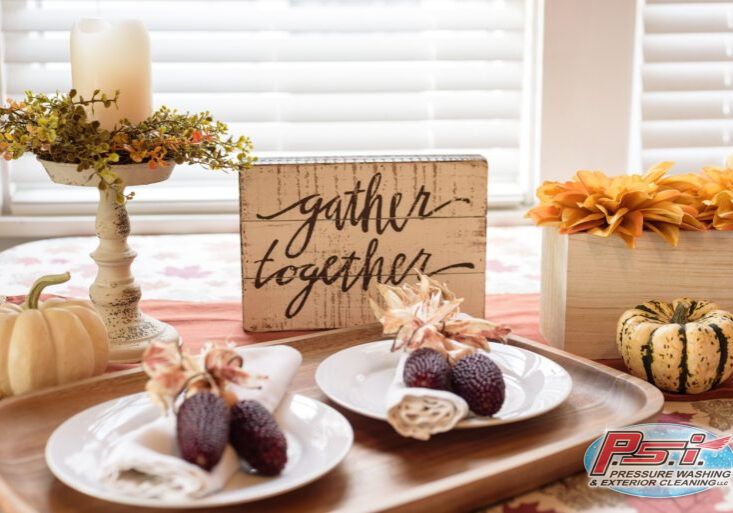 A cozy dining table setup for Thanksgiving featuring a "gather together" sign, decorative pumpkins, and dried corn on white plates. The table is adorned with a candle centerpiece and orange flowers, creating a warm, autumnal ambiance to help you prepare your home for the holiday season.